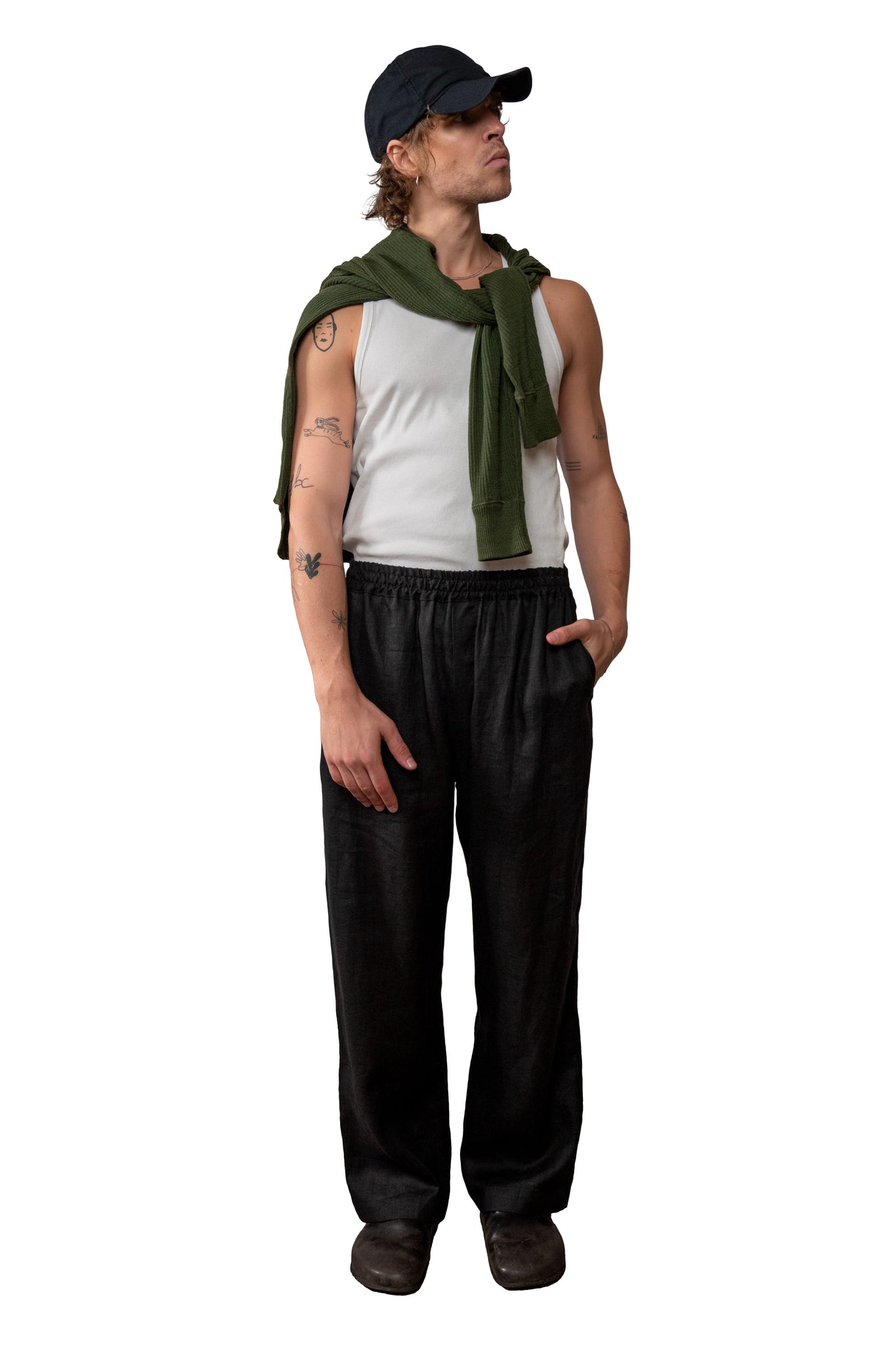 Person wearing a sleeveless top, black linen pants, and a green jumper on a white background